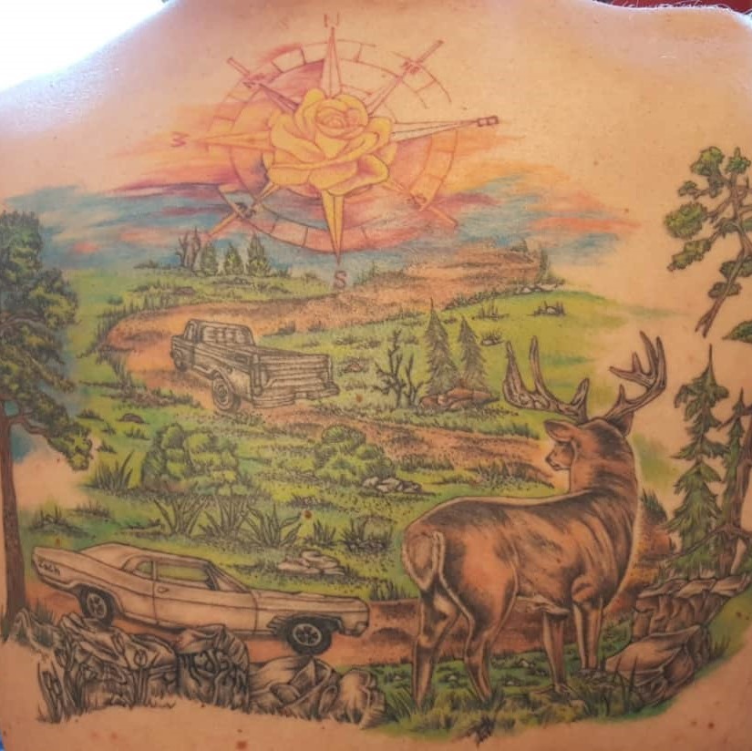 Tattoo of a colorful countryside landscape with cars, a compass, and a deer