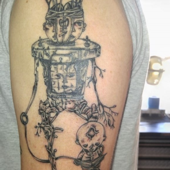 Tattoo of a tree-like person with a split head, a face on their stomach, and a grotesque toddler in front of it