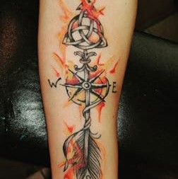 Tattoo of a colorful compass with an arrow through it