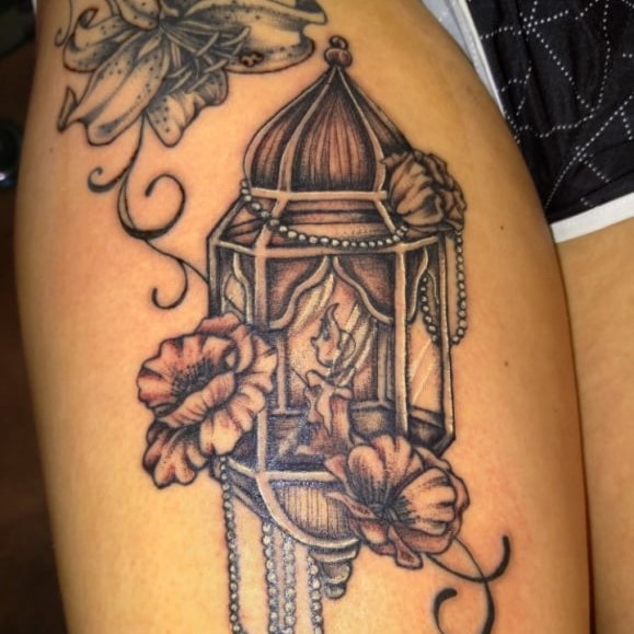 Tattoo of a candle in a cage, surrounded by a beaded necklace and some flowers